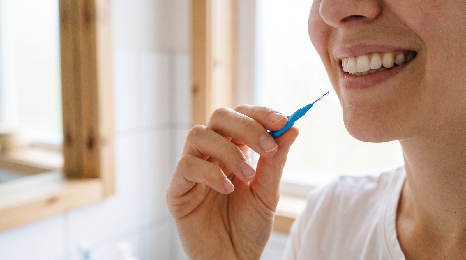 Main tenant une brossette interdentaire près d'un sourire aux dents saines